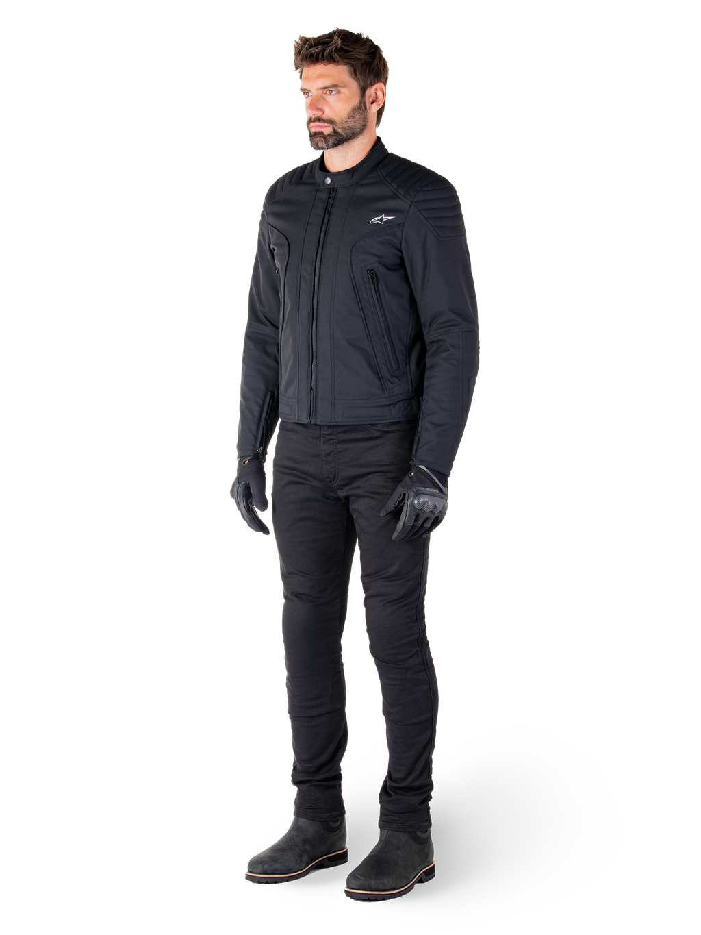 Pilota che indossa la giacca Alpinestars Clayton WR, giacca da moto urban nera, design slim-fit con dettagli trapuntati sulle spalle e finitura opaca, abbinata a pantaloni tecnici da guida e guanti neri.