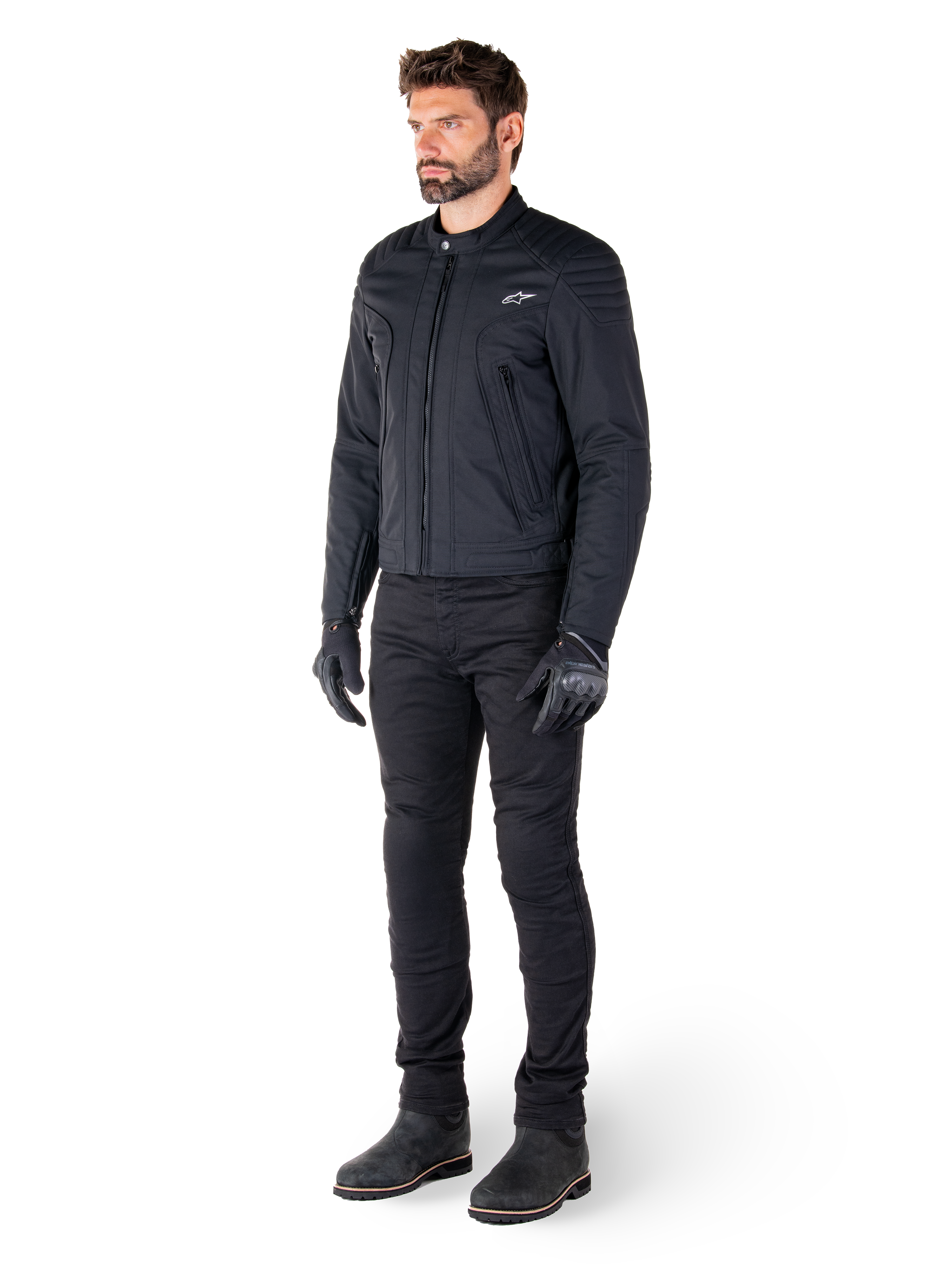 Pilota che indossa la giacca Alpinestars Clayton WR, giacca da moto urban nera, design slim-fit con dettagli trapuntati sulle spalle e finitura opaca, abbinata a pantaloni tecnici da guida e guanti neri.