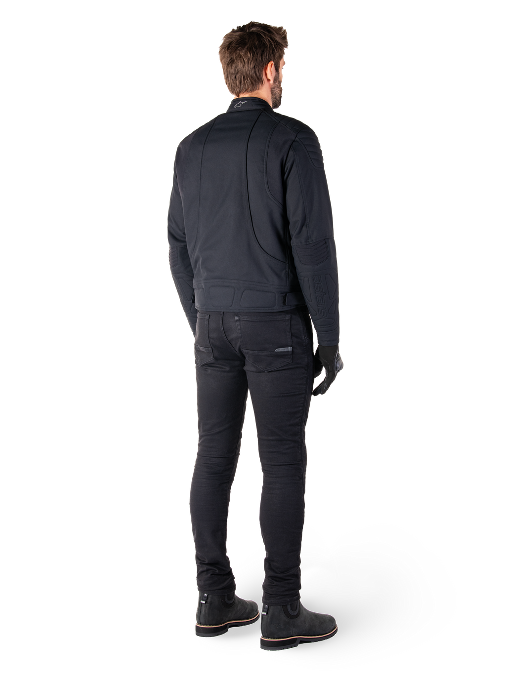 Vista posteriore di un pilota che indossa la giacca Alpinestars Clayton WR in nero, con pannelli trapuntati su gomiti e spalle, cuciture curve ergonomiche e dettagli riflettenti sul colletto, abbinata a pantaloni da moto e stivali neri per un look motociclistico urbano.