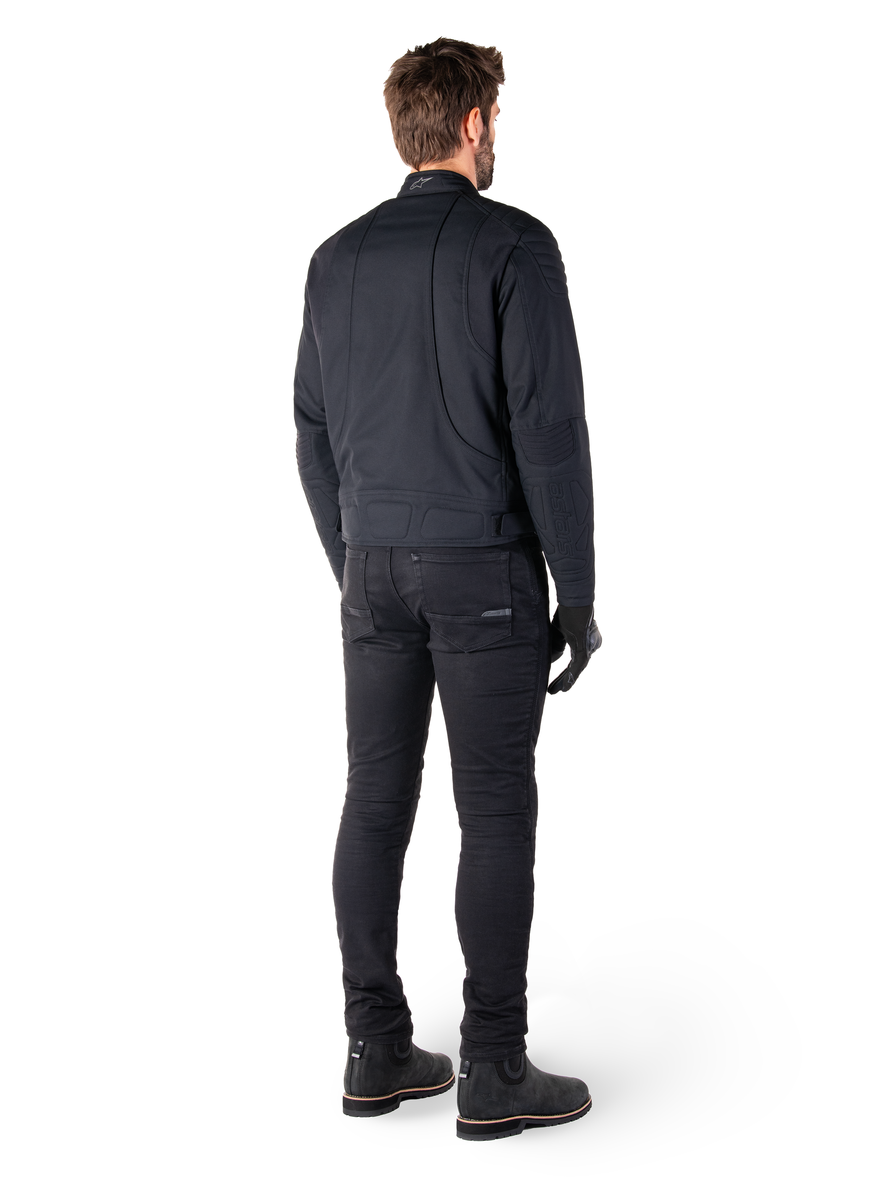 Vista posteriore di un pilota che indossa la giacca Alpinestars Clayton WR in nero, con pannelli trapuntati su gomiti e spalle, cuciture curve ergonomiche e dettagli riflettenti sul colletto, abbinata a pantaloni da moto e stivali neri per un look motociclistico urbano.