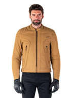 Alpinestars Clayton WR Jacket, giacca da moto urban, Utility Brown Light Gold, tessuto idrorepellente con spalle imbottite trapuntate, colletto alto da biker, dettagli con zip nere e logo sul petto, indossata con guanti protettivi e pantaloni neri