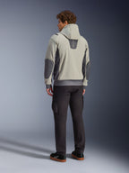 Modello visto di spalle che indossa la giacca Alpinestars Moblast Waterproof in Iron Gray Dark Sage, giacca da moto urbana con cappuccio con pannelli laterali grigio scuro e toppe rinforzate sui gomiti, abbinata a pantaloni da guida scuri e sneaker nere, estetica moderna e minimalista per il commuting urbano.