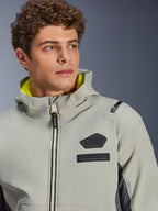 Giacca impermeabile Alpinestars Moblast, Iron Gray Dark Sage, primo piano di un modello maschile che indossa la giacca, con logo Alpinestars nero e patch MO.ST.EQ. sul petto, fodera del cappuccio giallo brillante e design tecnico moderno.