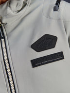 Giacca impermeabile Alpinestars Moblast, Iron Gray, dettaglio ravvicinato delle patch sul petto con logo Alpinestars e marchio MO.ST.EQ. Moto Streetwear Equipment, tessuto tecnico ripstop con robusta cerniera frontale e dettaglio della tasca sulla spalla.