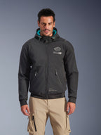 Alpinestars Moblast Waterproof Jacket, giacca da moto urbana da uomo, nera con fodera del cappuccio turchese, caratterizzata da tasche con zip 3D e design con cappuccio, indossata con pantaloni cargo beige, abbigliamento da moto urbano moderno