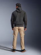 Alpinestars Moblast Waterproof Jacket, nero, vista posteriore di felpa da moto urbana con cappuccio, indossata con pantaloni cargo color sabbia e sneakers nere, design minimalista con marchio 'astars' verticale sulla parte superiore della schiena, abbigliamento tecnico da moto per ogni condizione atmosferica