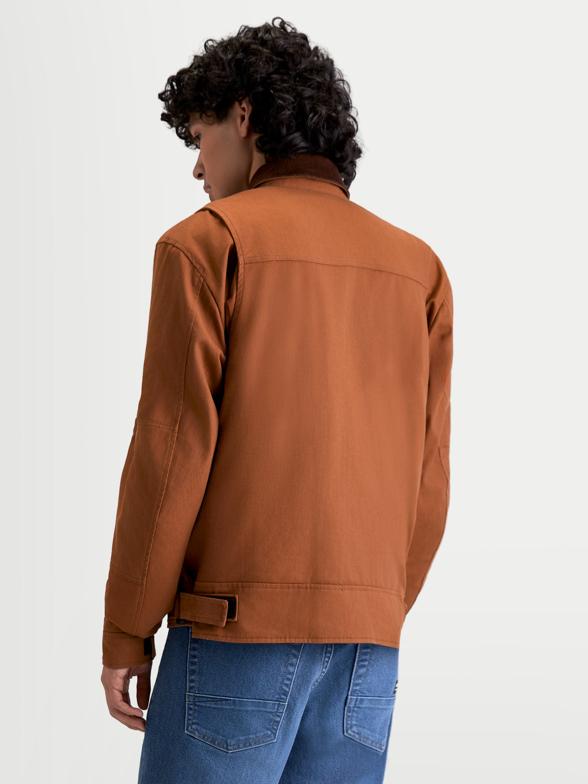 Alpinestars Mustang Wp Giacca, giacca da moto urbana contemporanea da uomo in marrone ruggine e marrone scuro, vista posteriore a tre quarti su un modello che mostra la struttura in twill elasticizzato in stile workwear e i dettagli a soffietto sulle spalle