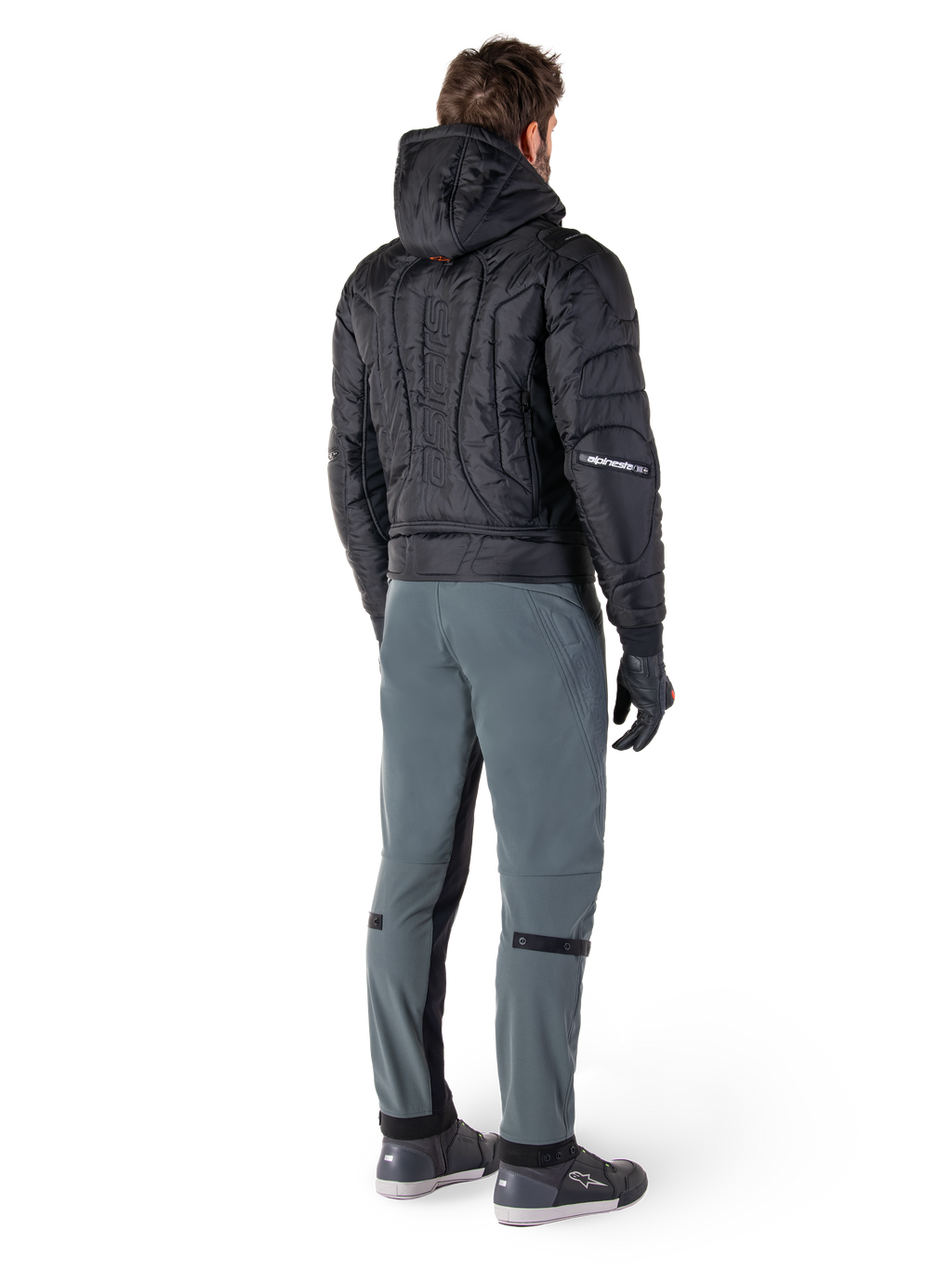 Alpinestars Mohobbs Waterproof Jacket, nero, vista posteriore di un bomber trapuntato imbottito con marchio verticale a rilievo sulla schiena, abbinato a pantaloni da guida grigi e guanti neri, abbigliamento da moto ispirato allo streetwear urbano