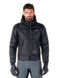 Alpinestars Mohobbs Waterproof Jacket, giacca da moto bomber imbottita nera, tessuto in poliestere trapuntato con cerniera frontale e tasche con zip, piccolo logo bianco sul petto, indossata da un modello con pantaloni grigi e guanti, design urban streetwear per la guida in città.