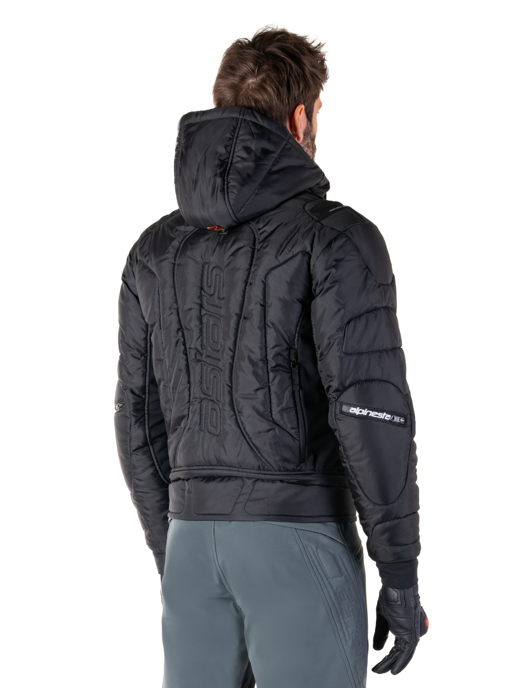 Alpinestars Mohobbs Waterproof Jacket, nero, vista posteriore con costruzione trapuntata imbottita, cappuccio, marchio astars verticale sulla schiena e logo Alpinestars sulle maniche, indossata con pantaloni grigi e guanti neri