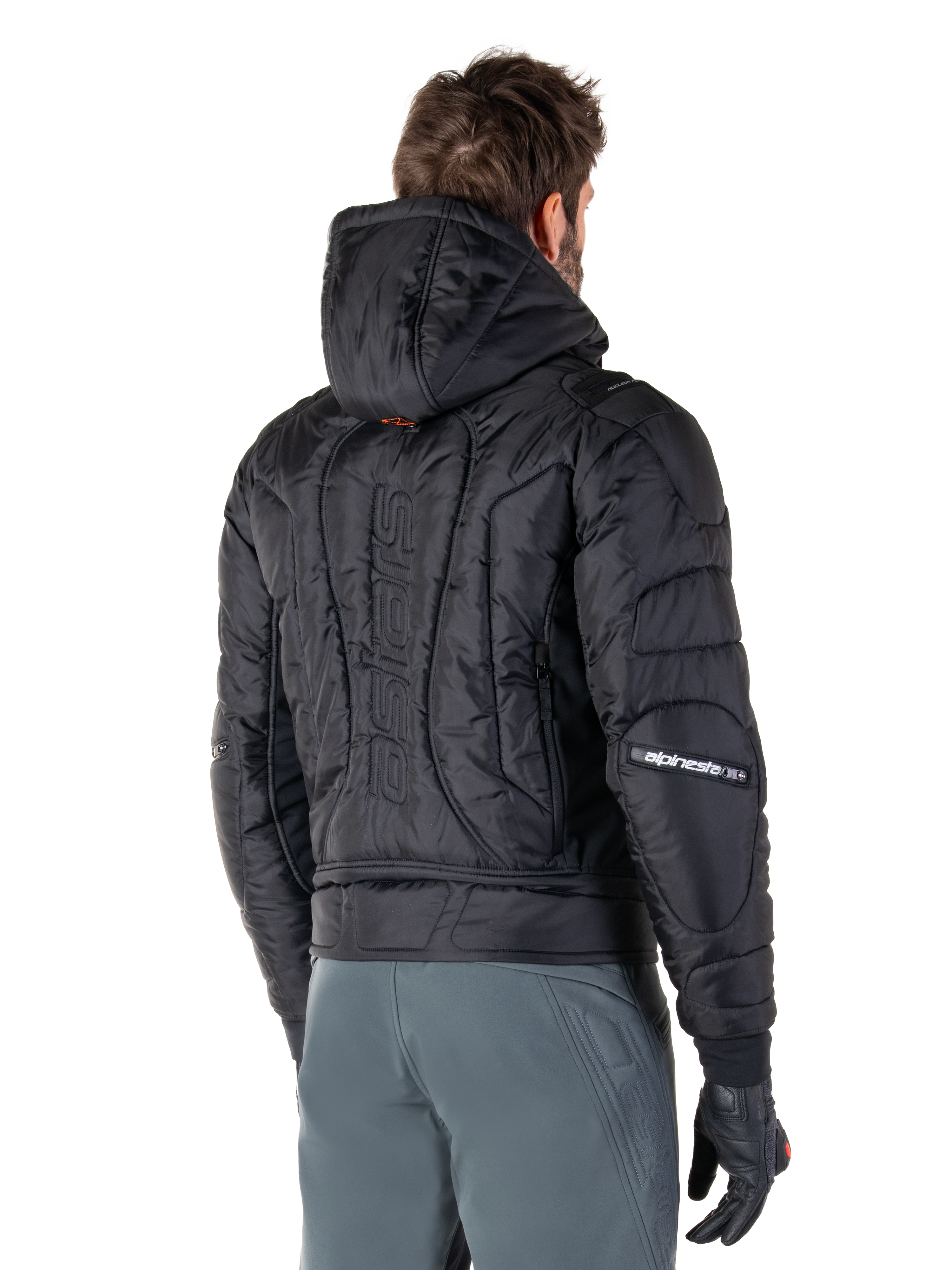 Alpinestars Mohobbs Waterproof Jacket, nero, vista posteriore con costruzione trapuntata imbottita, cappuccio, marchio astars verticale sulla schiena e logo Alpinestars sulle maniche, indossata con pantaloni grigi e guanti neri