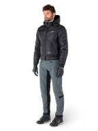 Alpinestars Mohobbs Waterproof Jacket, bomber da moto urban trapuntato nero con cappuccio, indossata da un modello con pantaloni da guida grigi e guanti neri, con logo bianco sul petto, abbigliamento protettivo contemporaneo d'ispirazione streetwear