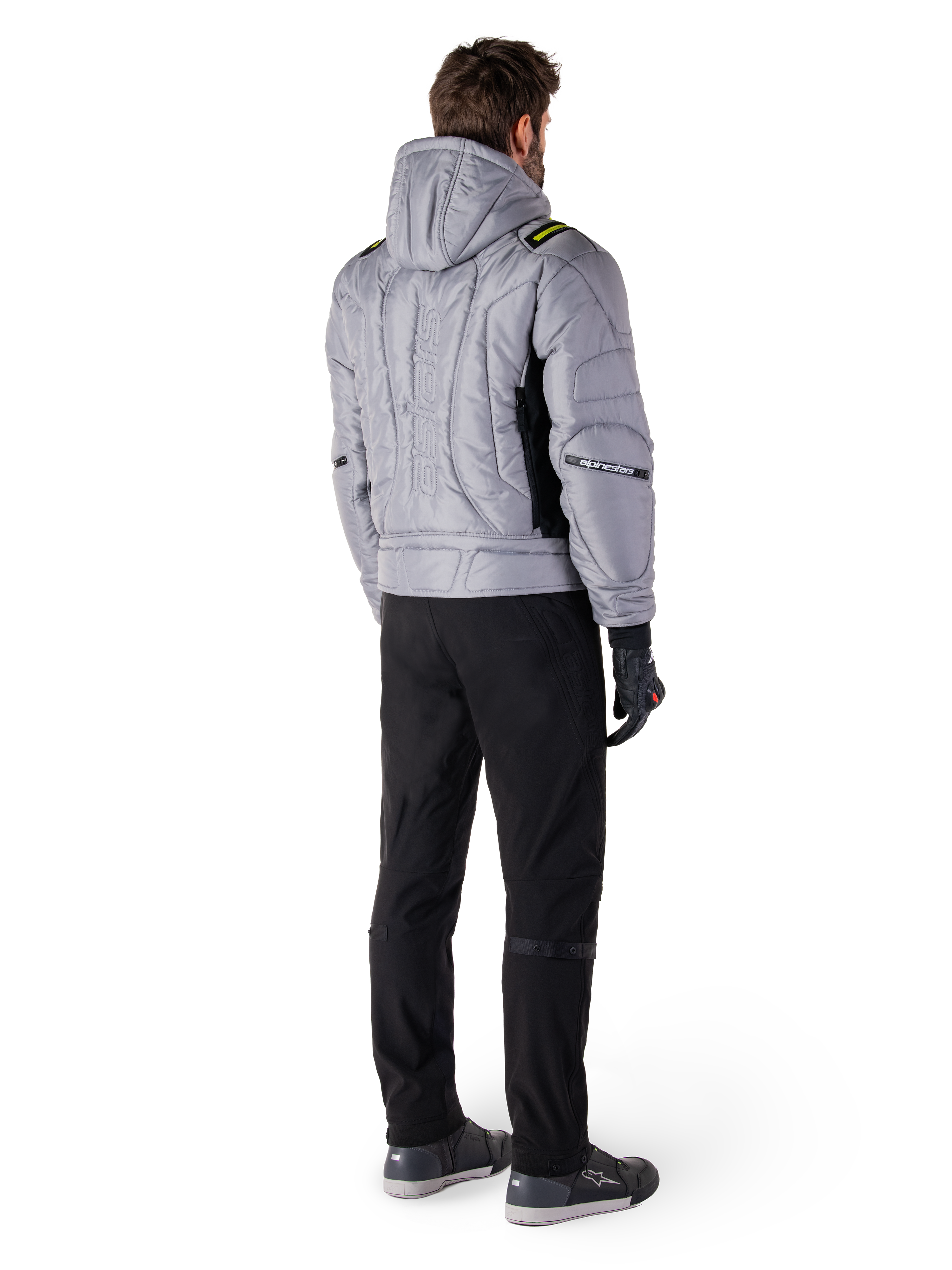 Giacca Alpinestars Mohobbs Waterproof, Lunar Gray Lime Punch, vista posteriore di giacca da moto in stile bomber trapuntata con cappuccio, con scritta Alpinestars sul retro, indossata con pantaloni da guida e guanti neri, streetwear urbano da moto