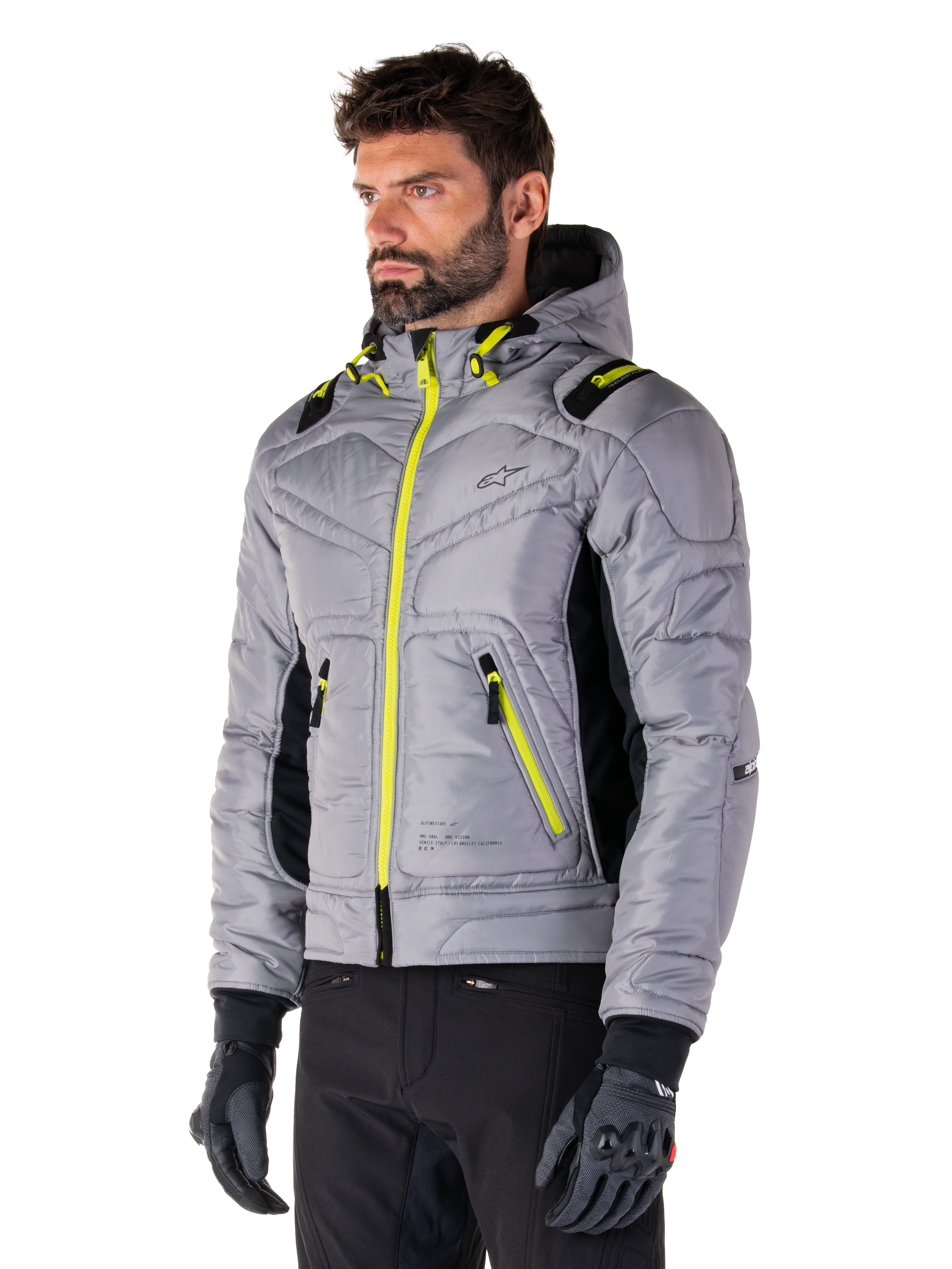 Giacca Alpinestars Mohobbs Waterproof, Lunar Gray Lime Punch, giacca da moto bomber trapuntata da uomo con cerniere e dettagli coulisse giallo neon, indossata con pantaloni da guida e guanti neri, design moderno urban moto streetwear con profilo con cappuccio