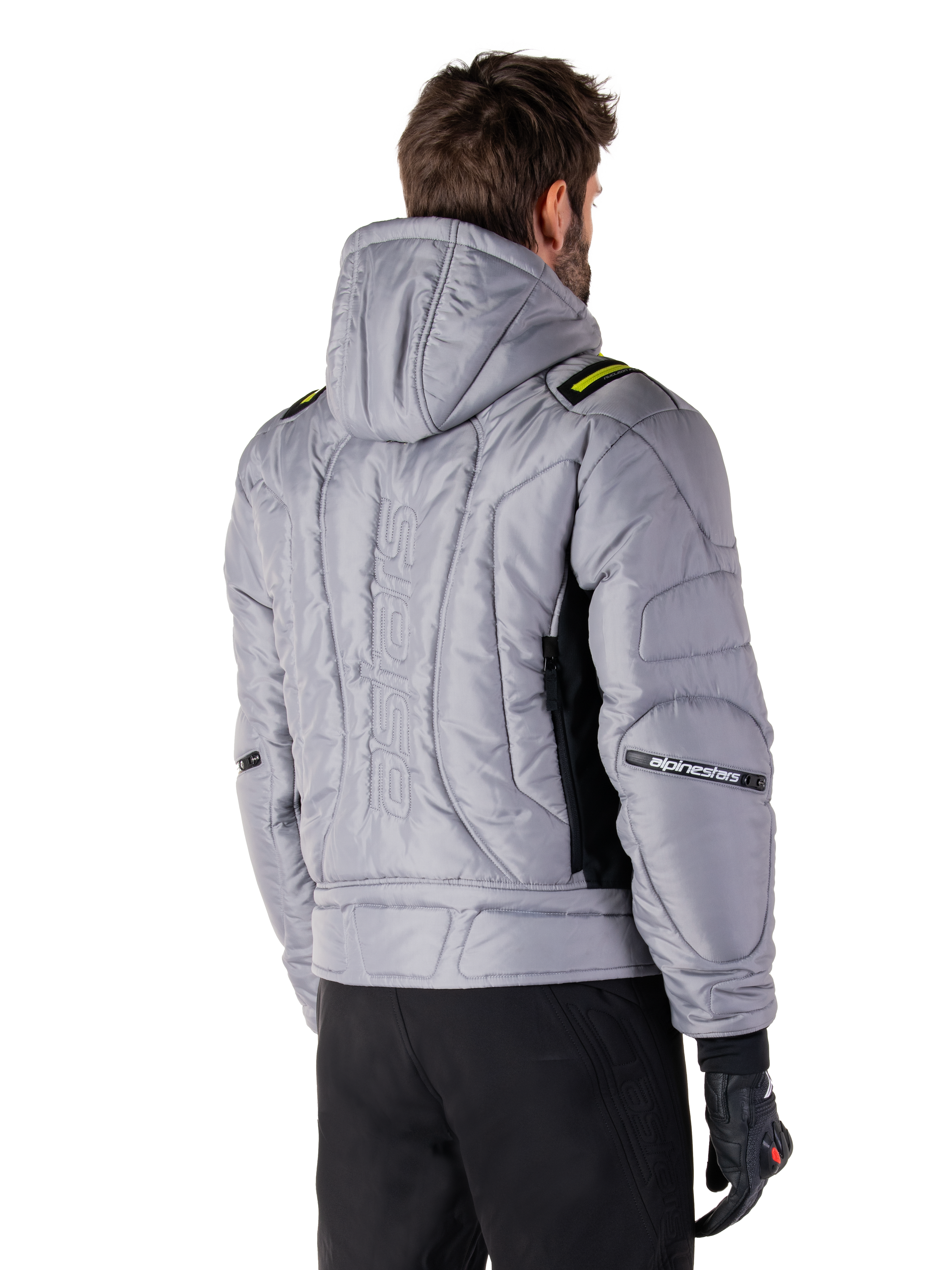Giacca Alpinestars Mohobbs Waterproof in grigio e verde lime, vista posteriore su un modello, design bomber imbottito e trapuntato con marchio astars goffrato in verticale sul retro, dettagli verde lime sulle spalle, con cappuccio, indossata con pantaloni da moto e guanti neri.