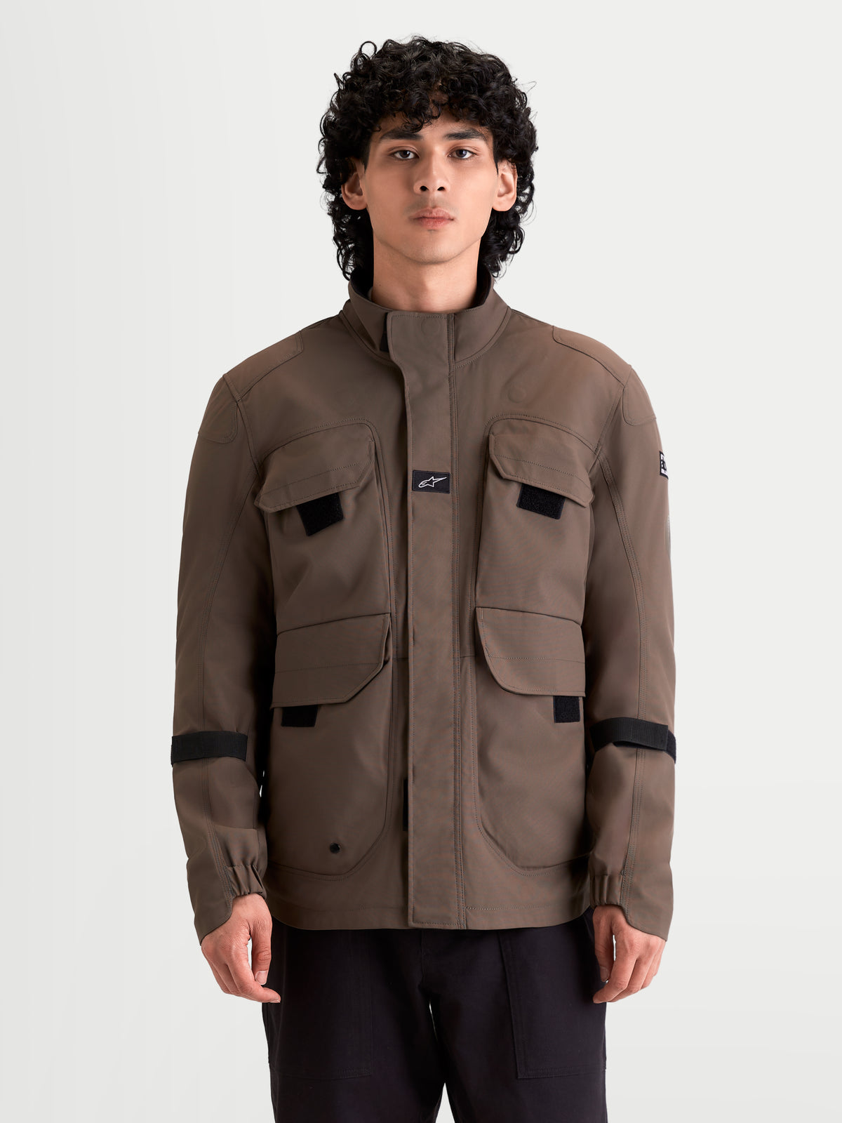 Alpinestars Altan Drystar Giacca, giacca da moto urbana contemporanea impermeabile da uomo in marrone noce, vista frontale indossata da un modello che mostra le tasche portaoggetti in stile field-jacket e il collo caldo