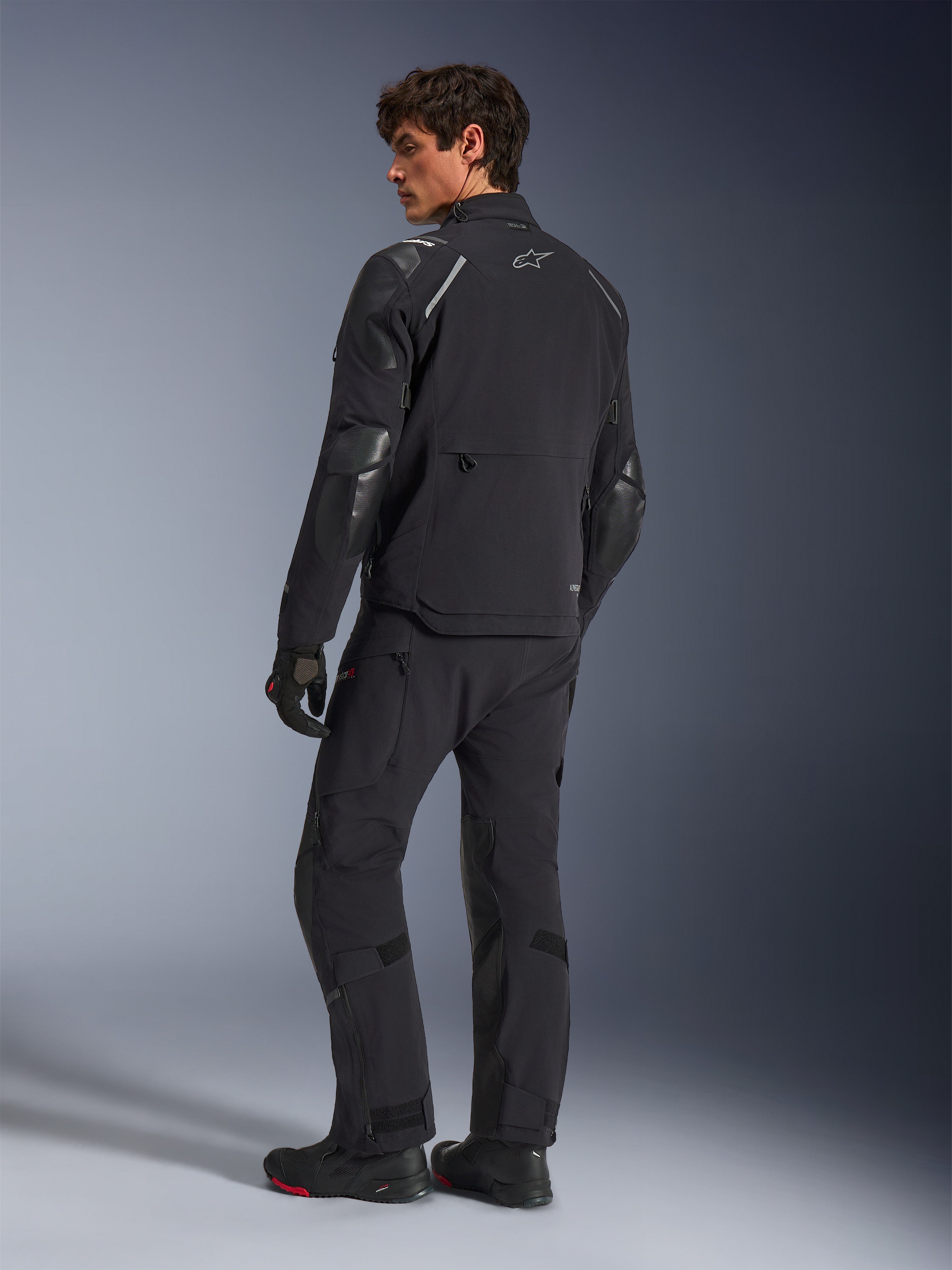 Giacca Alpinestars Andes Pro Drystar® XF, giacca da moto adventure, nero, vista posteriore indossata con pantaloni e stivali abbinati, con pannelli rinforzati e logo a stella argento, abbigliamento tecnico da moto per tutte le stagioni