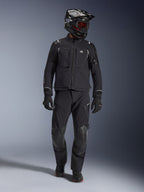 Pilota adventure che indossa la giacca Alpinestars Andes Pro Drystar® XF in nero e grigio scuro, pantaloni adventure neri coordinati, casco bianco e nero con maschera rossa, guanti e stivali neri; presenta ampie tasche anteriori, dettagli riflettenti e costruzione tecnica laminata a 3 strati per il turismo in ogni condizione climatica.