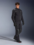 Giacca Alpinestars Andes Pro Drystar® XF, giacca da moto nera e grigio scuro, indossata da un modello con pantaloni adventure coordinati, guanti e stivali, scatto in studio a figura intera, abbigliamento tecnico da touring adventure con dettagli riflettenti e branding