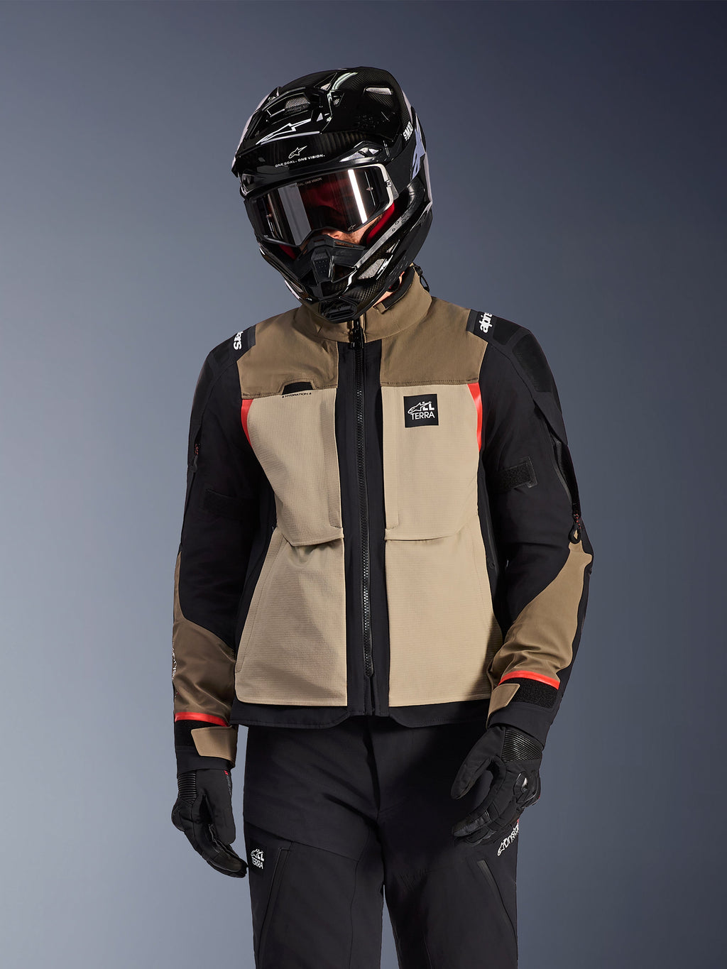 Giacca Alpinestars Andes Pro Drystar® XF, giacca da moto adventure touring, beige noce e marrone con pannelli neri e dettagli rossi, indossata con casco e occhiali Alpinestars neri, abbigliamento tecnico da moto.