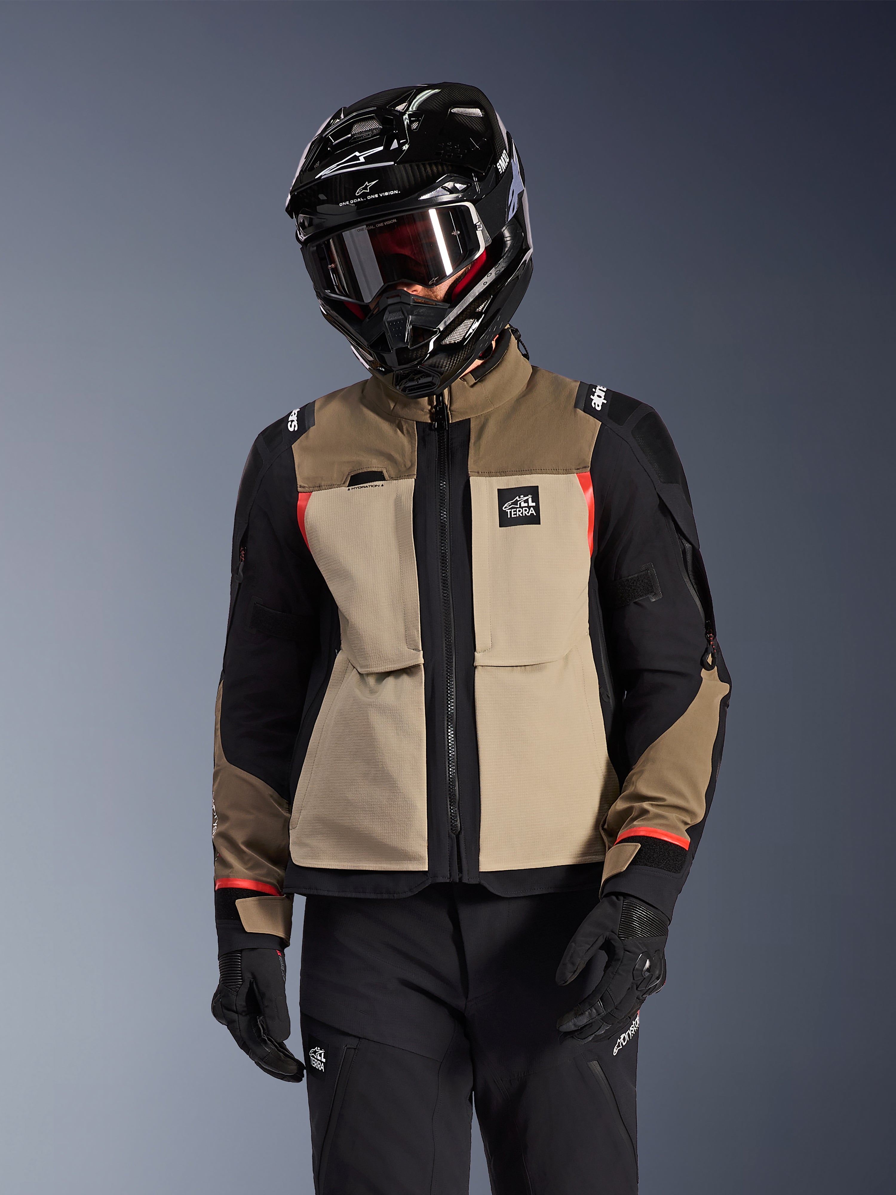 Giacca Alpinestars Andes Pro Drystar® XF, giacca da moto adventure touring, beige noce e marrone con pannelli neri e dettagli rossi, indossata con casco e occhiali Alpinestars neri, abbigliamento tecnico da moto.