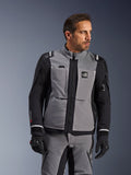 Giacca Alpinestars Andes Pro Drystar® XF in grigio scuro e nero, abbigliamento per guida adventure, indossata da un uomo con pantaloni grigi coordinati e guanti neri, con guscio laminato a 3 strati, tasche utility e logo 'Terra' sul petto