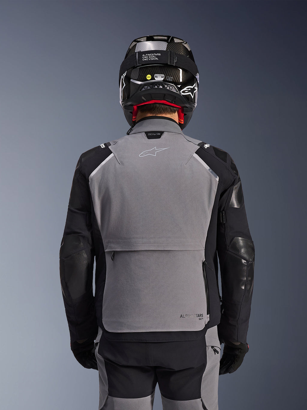 Giacca Alpinestars Andes Pro Drystar® XF, grigio scuro e nero, vista posteriore con ampia tasca posteriore portaoggetti e marchio Tech-Air, indossata da un pilota con casco nero e pantaloni da moto coordinati, abbigliamento professionale da touring adventure