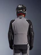Giacca Alpinestars Andes Pro Drystar® XF, grigio scuro e nero, vista posteriore con ampia tasca posteriore portaoggetti e marchio Tech-Air, indossata da un pilota con casco nero e pantaloni da moto coordinati, abbigliamento professionale da touring adventure