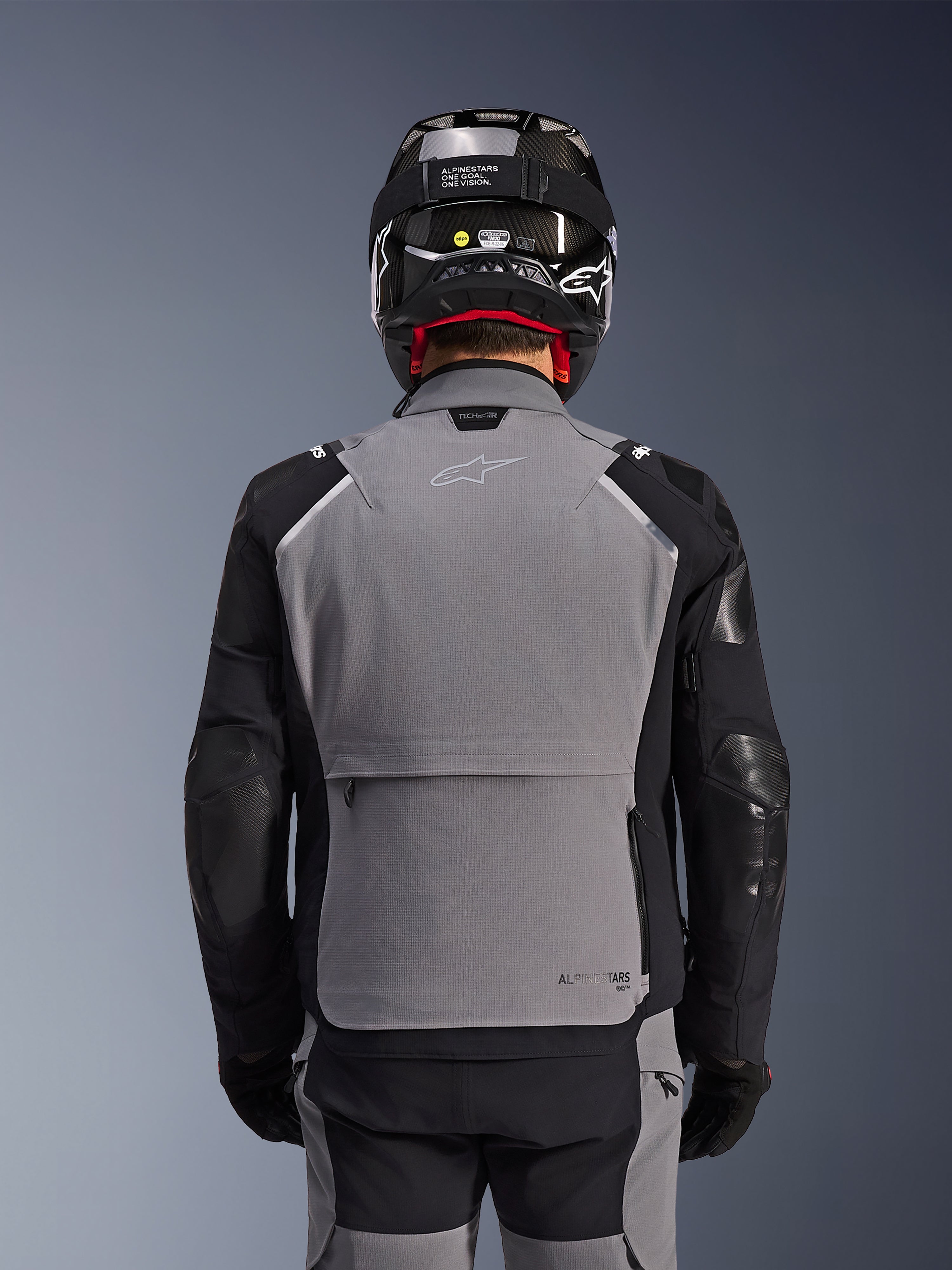Giacca Alpinestars Andes Pro Drystar® XF, grigio scuro e nero, vista posteriore con ampia tasca posteriore portaoggetti e marchio Tech-Air, indossata da un pilota con casco nero e pantaloni da moto coordinati, abbigliamento professionale da touring adventure