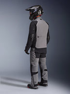 Giacca Alpinestars Andes Pro Drystar® XF, giacca da moto adventure, grigio scuro e nero, vista posteriore con pannello posteriore grigio e maniche nere, indossata con pantaloni coordinati e casco nero, abbigliamento tecnico per ogni condizione climatica