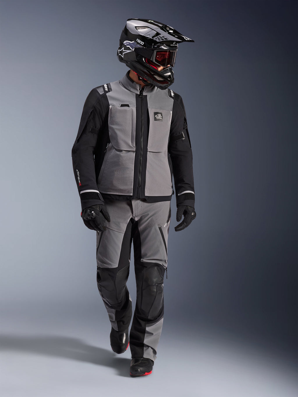 Motociclista adventure con giacca Alpinestars Andes Pro Drystar® XF in grigio scuro e nero, pantaloni adventure coordinati, casco Alpinestars nero con maschera, guanti e stivali neri, abbigliamento tecnico da touring completo per lunghi viaggi