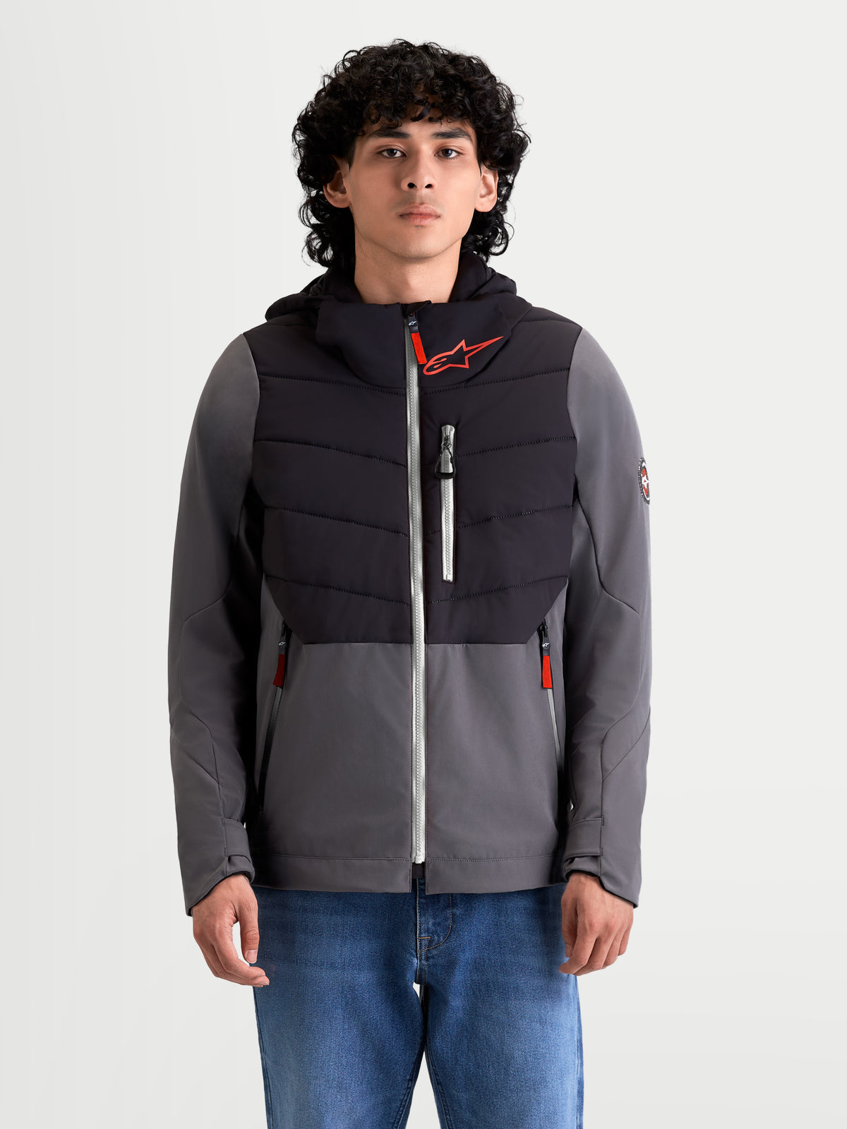 Alpinestars Giacca Therma-Tech Impermeabile, giacca da moto urbana da uomo in nero e grigio scuro, vista frontale su un modello con jeans, caratterizzata da costruzione trapuntata saldata a sonoro, membrana impermeabile e cappuccio integrato