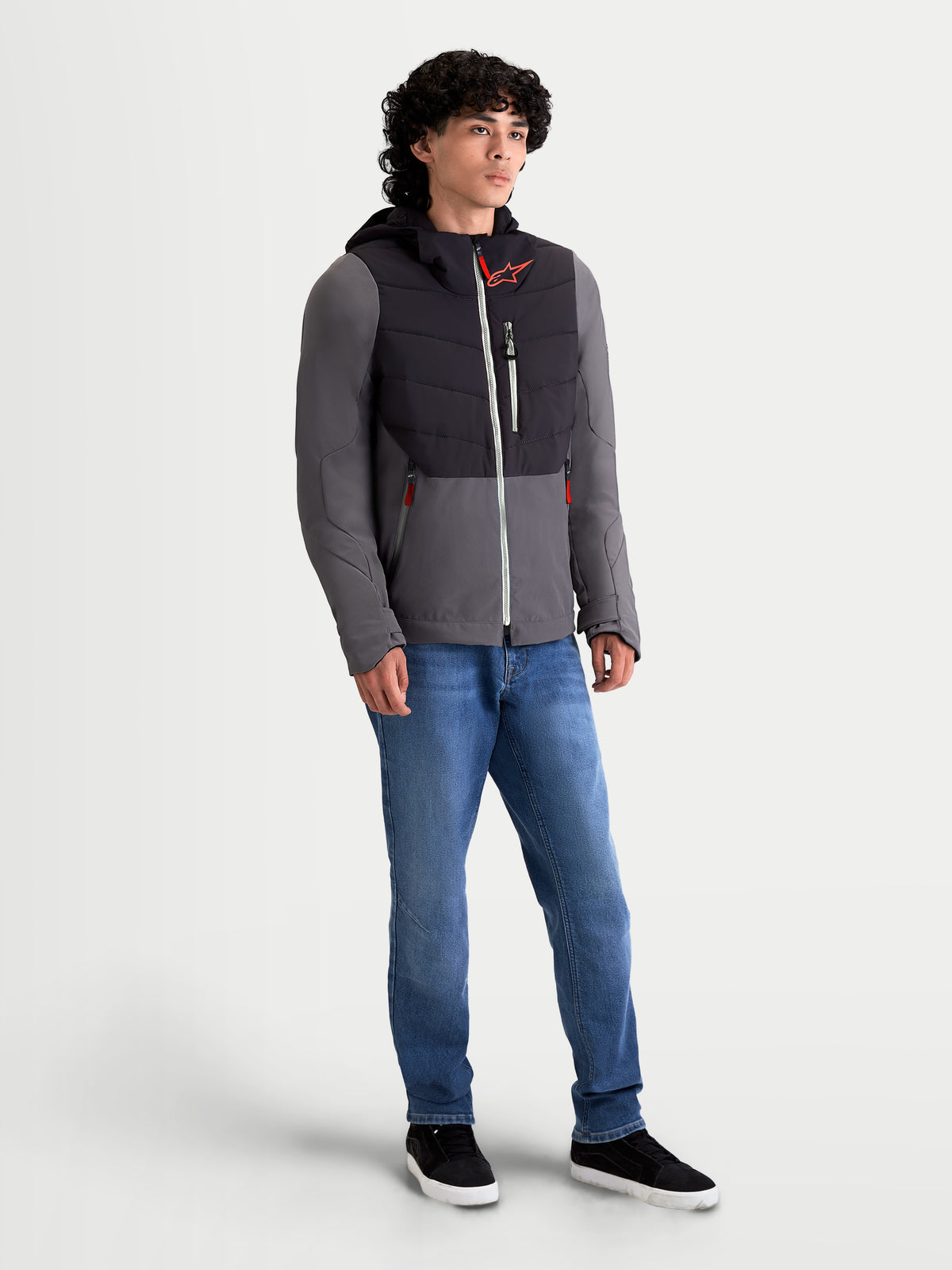 Alpinestars Giacca Therma-Tech Impermeabile, giacca da moto urbana contemporanea da uomo in nero e grigio scuro, vista frontale a tre quarti indossata da un modello con sistema di cappuccio integrato e costruzione trapuntata saldata a ultrasuoni