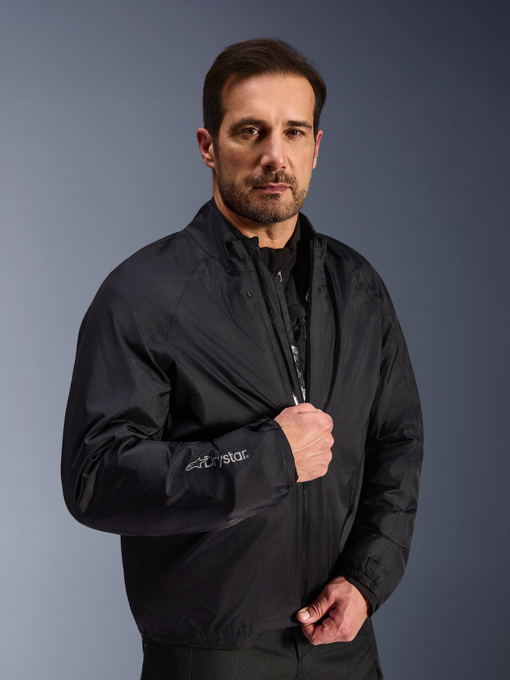 Giacca Alpinestars Cusco Drystar®, strato impermeabile nero indossato da un modello, logo Drystar sulla manica, abbigliamento da moto leggero per adventure touring