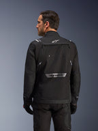 Pilota visto da dietro che indossa la giacca Alpinestars Cusco Drystar® in nero, giacca in tessuto adventure touring con ampia tasca posteriore e loghi riflettenti, abbinata a pantaloni e guanti neri coordinati