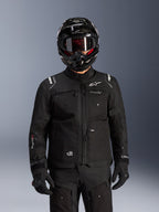 Giacca Alpinestars Cusco Drystar®, giacca da moto adventure touring nera, indossata con casco integrale adventure nero e occhiali scuri, con numerose tasche utility, logo Alpinestars sul petto e logo Drystar® sulla manica, parte di un completo road adventure.