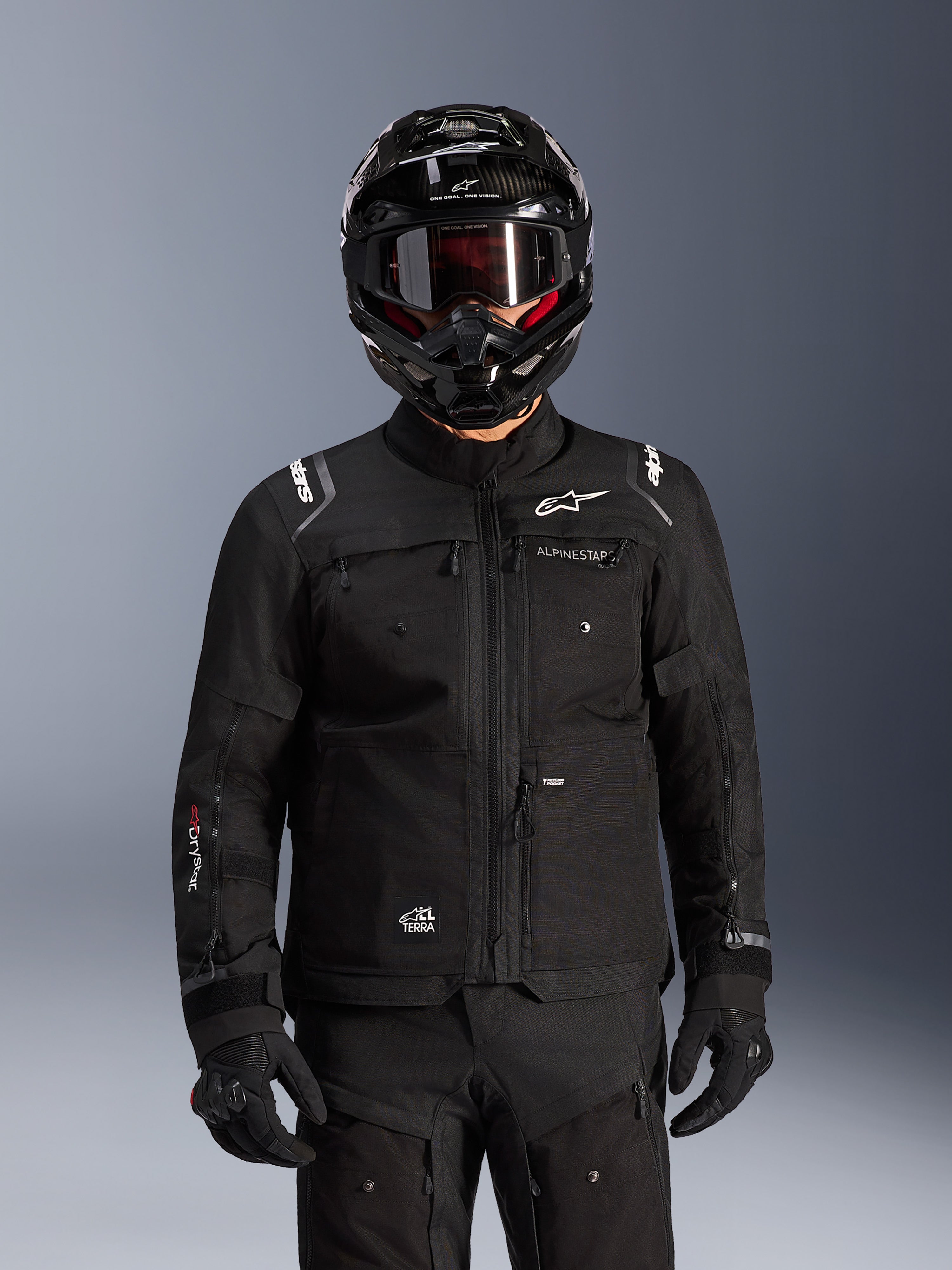 Giacca Alpinestars Cusco Drystar®, giacca da moto adventure touring nera, indossata con casco integrale adventure nero e occhiali scuri, con numerose tasche utility, logo Alpinestars sul petto e logo Drystar® sulla manica, parte di un completo road adventure.