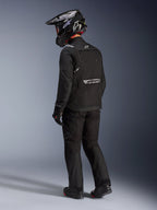 Giacca Alpinestars Cusco Drystar® in nero, vista posteriore-laterale di un pilota con kit completo da adventure touring, inclusi pantaloni e guanti neri coordinati, casco adventure nero, costruzione in tessuto con marchio riflettente sulla schiena