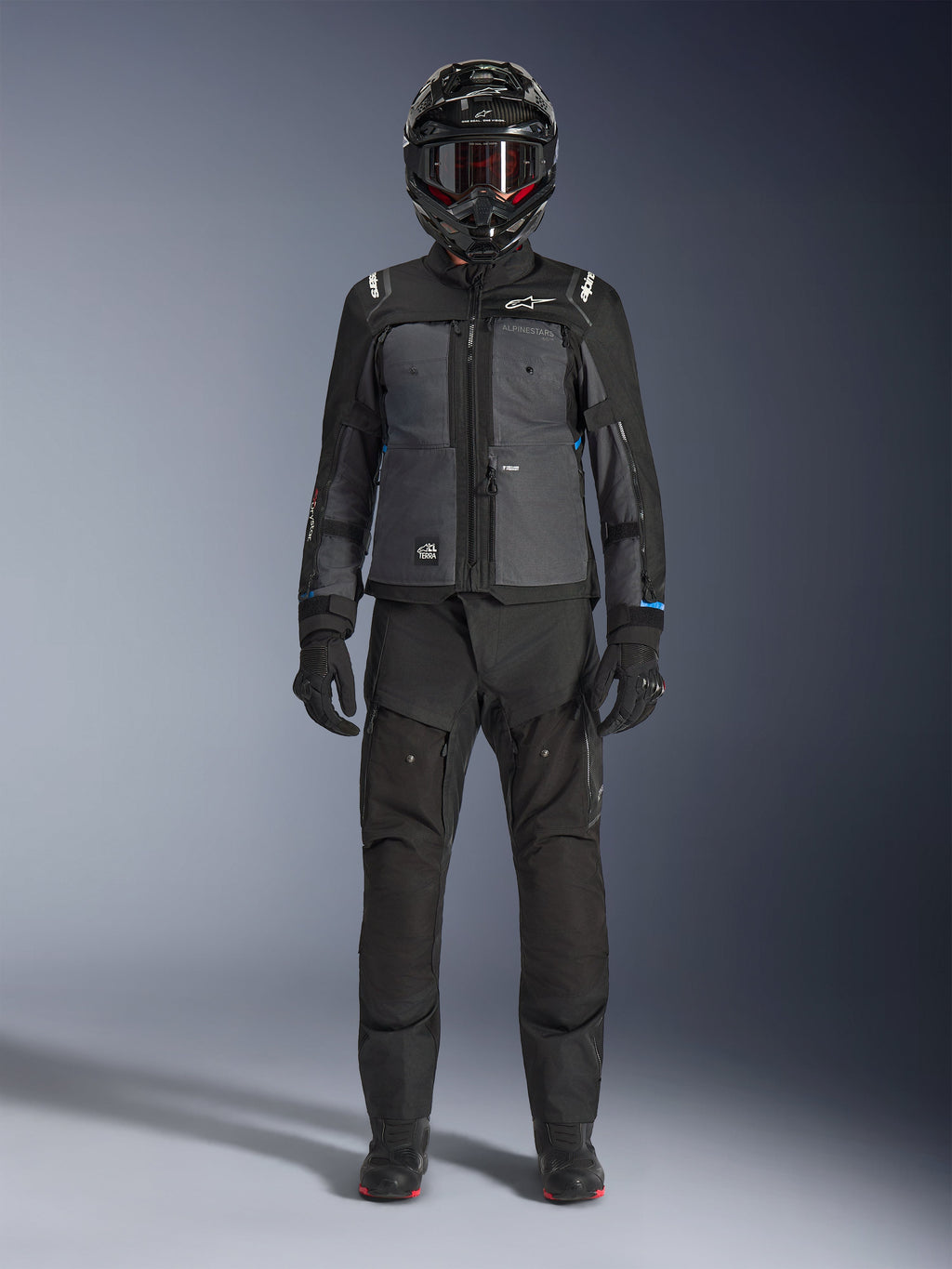 Giacca Alpinestars Cusco Drystar®, giacca da adventure touring in nero e grigio scuro, indossata con pantaloni neri coordinati, guanti e casco integrale, vista frontale a figura intera, abbigliamento protettivo da moto