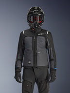 Giacca Alpinestars Cusco Drystar®, Nero e Grigio Scuro, giacca da moto adventure touring indossata con pantaloni tecnici neri abbinati e un casco dual-sport, caratterizzata da un design bicolore con pannelli in ripstop e branding Alpinestars