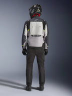 Motociclista visto da dietro che indossa la giacca Alpinestars Cusco Drystar® in Ice Gray, Mid Gray e Deep Gray, con un ampio pannello di ventilazione posteriore e logo Alpinestars, abbinata a pantaloni da moto neri e un casco nero, abbigliamento da moto adventure touring