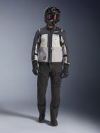 Giacca Alpinestars Cusco Drystar®, Ice Gray Mid Gray Deep Gray, giacca da moto adventure indossata con pantaloni da guida neri, guanti neri e casco nero con occhiali, caratterizzata da pannelli grigi color-block e dettagli tecnici per il touring su strada e adventure.