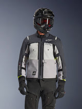 Giacca Alpinestars Cusco Drystar®, giacca da adventure touring, colorazione Ice Gray, Mid Gray e Deep Gray, caratterizzata da pannelli grigi multi-tonali, prese d'aria con cerniera sul petto e logo Alpinestars, indossata da un motociclista con casco nero e occhiali.