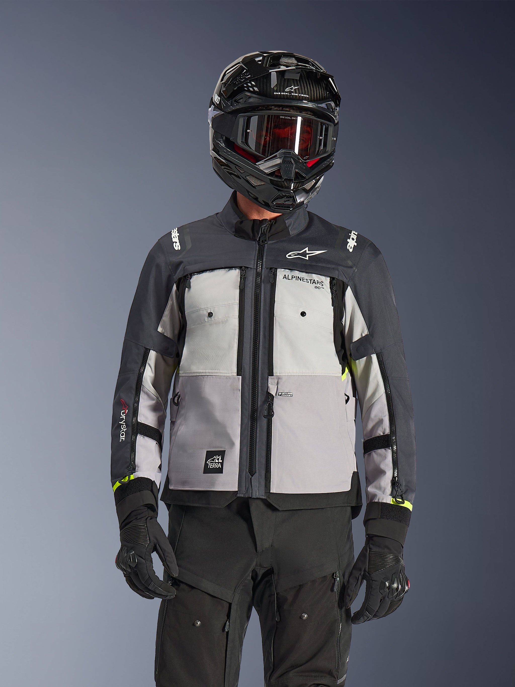 Giacca Alpinestars Cusco Drystar®, giacca da adventure touring, colorazione Ice Gray, Mid Gray e Deep Gray, caratterizzata da pannelli grigi multi-tonali, prese d'aria con cerniera sul petto e logo Alpinestars, indossata da un motociclista con casco nero e occhiali.