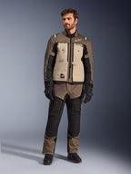 Giacca Alpinestars Cusco Drystar® in Walnut Aluminum Black, indossata da un motociclista con pantaloni adventure touring abbinati, guanti e stivali neri, con pannelli sul petto color sabbia, maniche nere con sottili accenti arancioni e cerniere di ventilazione funzionali per la guida su strada.