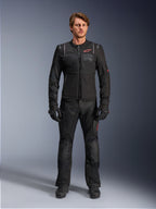 Modello con giacca Alpinestars ST-2 Air, giacca da moto nera con pannelli in mesh e logo rosso, scritta 'Alpinestars Exploration Equipment' sul petto, abbinata a pantaloni tecnici da guida e guanti neri, equipaggiamento moderno per adventure touring