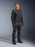 Modello che indossa la giacca Alpinestars ST-2 Air in nero, con logo a stella rosso e marchio 'Alpinestars Exploration Equipment', abbinata a pantaloni da moto, guanti e stivali neri coordinati per un moderno outfit da touring estivo.