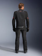 Giacca Alpinestars ST-2 Air, nero, vista posteriore di un pilota che indossa la giacca da moto e pantaloni neri abbinati, con pannelli di ventilazione in mesh, logo rosso sulla parte superiore della schiena e marchio Alpinestars grigio sul bordo inferiore posteriore