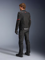 Giacca Alpinestars ST-2 Air, giacca da moto nera, vista posteriore su modello con logo a stella rosso sulla parte superiore della schiena e marchio Alpinestars riflettente in vita, abbinata a pantaloni tecnici da moto e guanti neri coordinati.