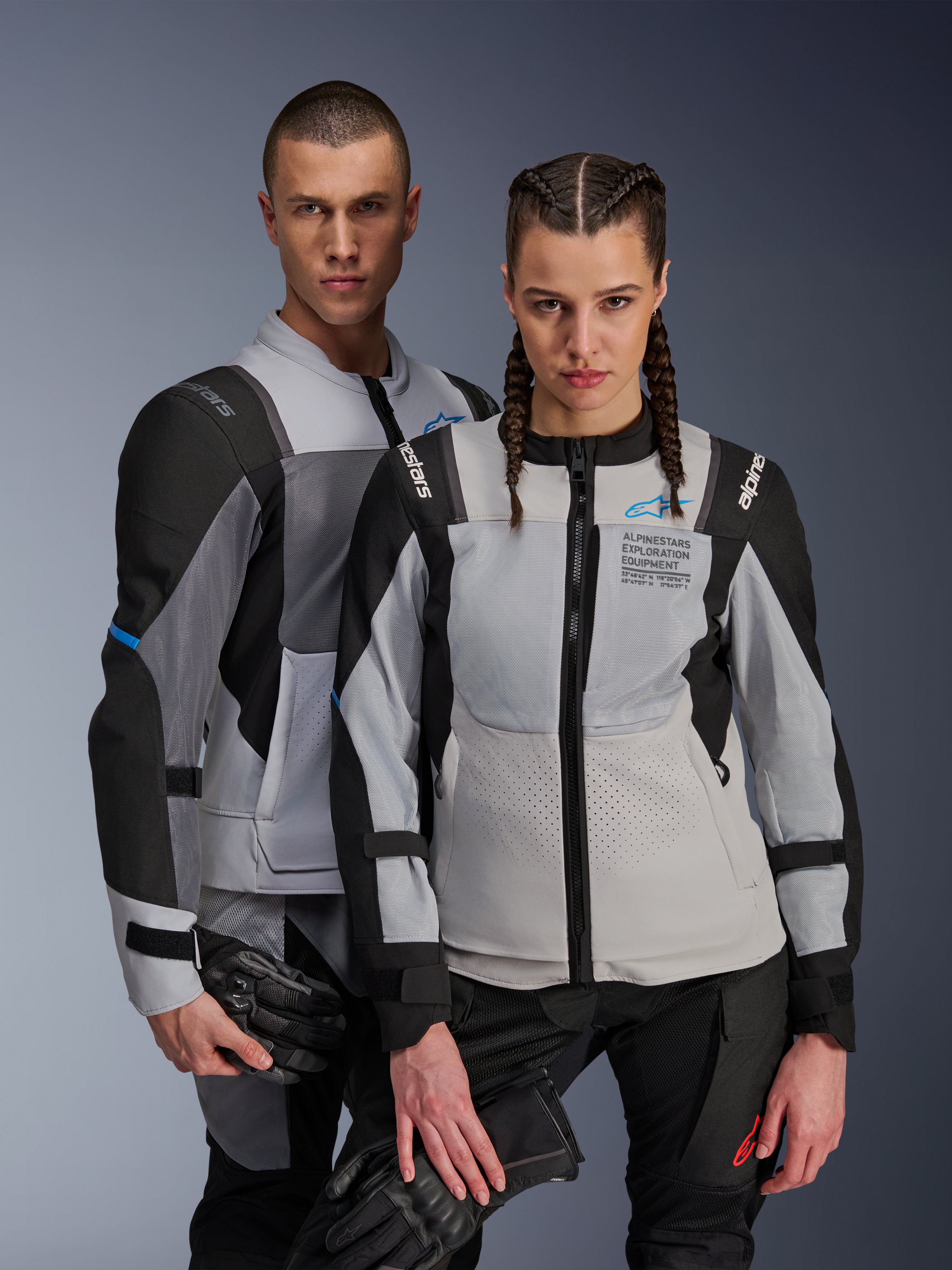 Giacche Alpinestars ST-2 Air, giacche da moto in tessuto, Ice Gray Dark Gray Black, coppia che indossa abbigliamento adventure touring coordinato con pannelli di ventilazione in rete e marchio Alpinestars Exploration Equipment, con guanti da moto